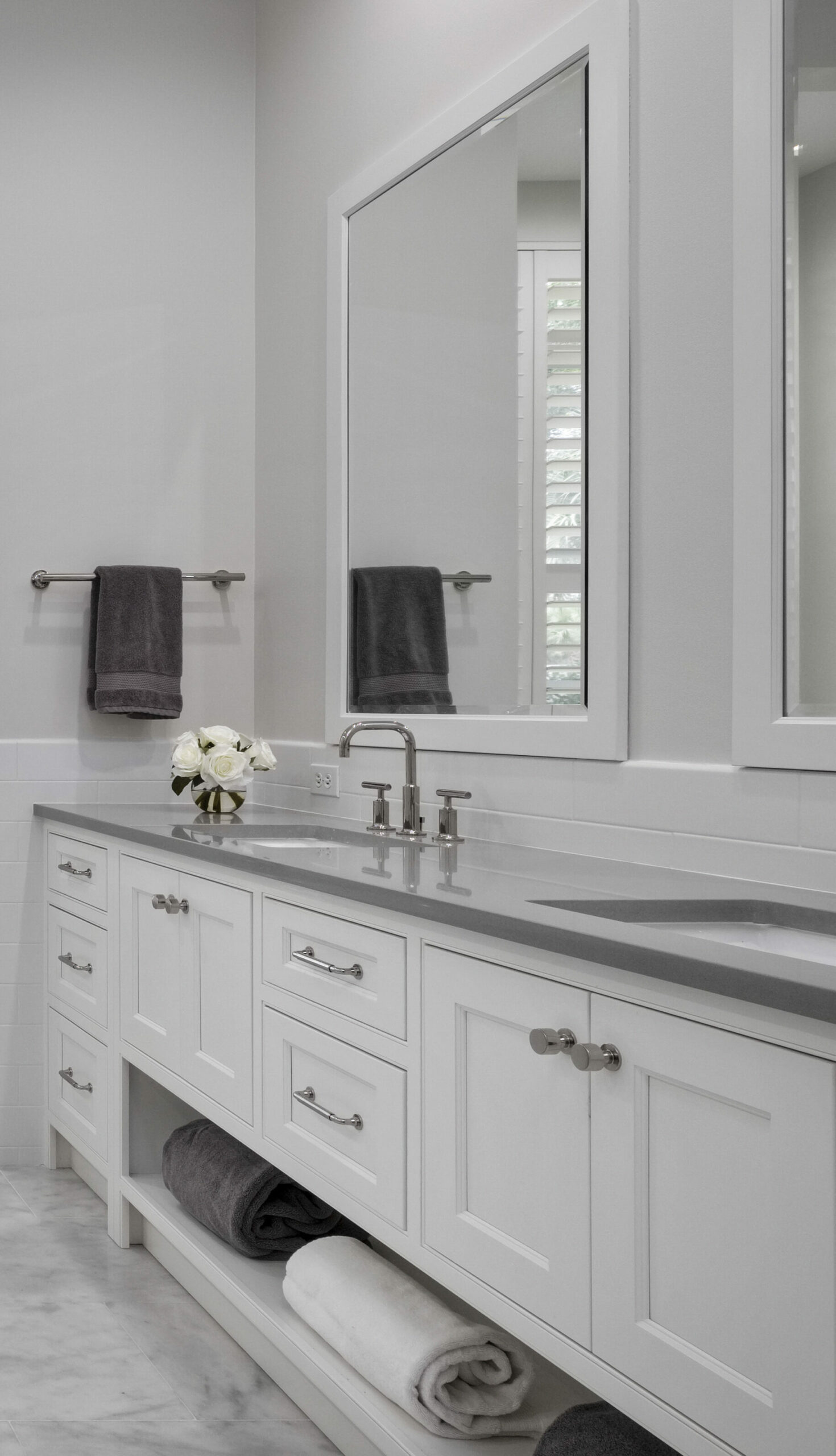 Semi-custom white inset bathroom cabinets. There is stainless steel hardware on the cabinets. The walls are white and the mirror frames are also white.