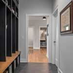 Picture shows a small hallway mudroom that has black, built-in lockers. There are no doors on the cubbies of the locker, but they do feature traditional hooks with baskets underneath an bench.