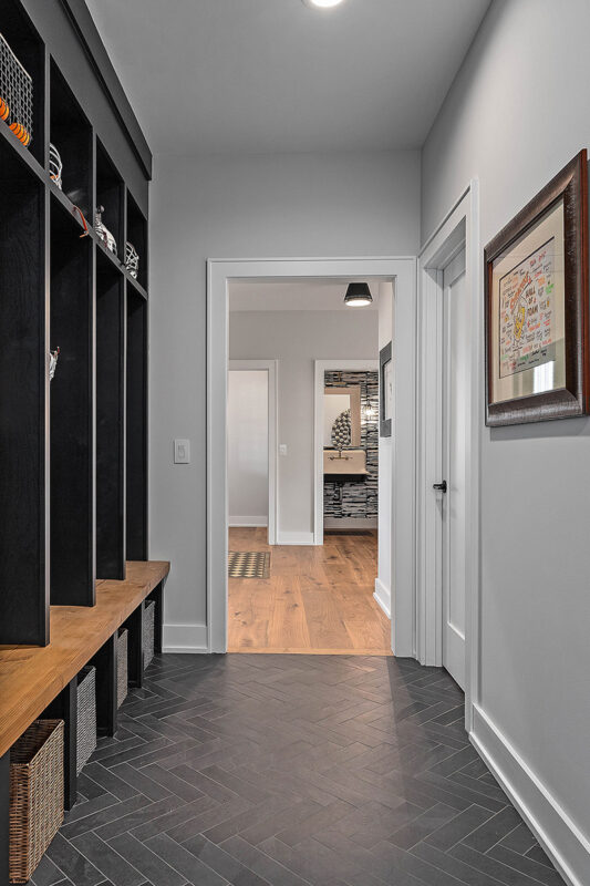 Picture shows a small hallway mudroom that has black, built-in lockers. There are no doors on the cubbies of the locker, but they do feature traditional hooks with baskets underneath an bench.