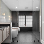 dark grey bathroom tile with an accent black subway tiled wall. in the middle of the black wall there is a large window that has frosted glass.