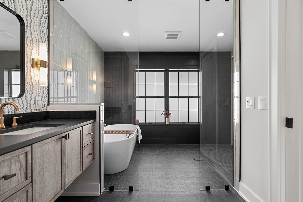 dark grey bathroom tile with an accent black subway tiled wall. in the middle of the black wall there is a large window that has frosted glass.