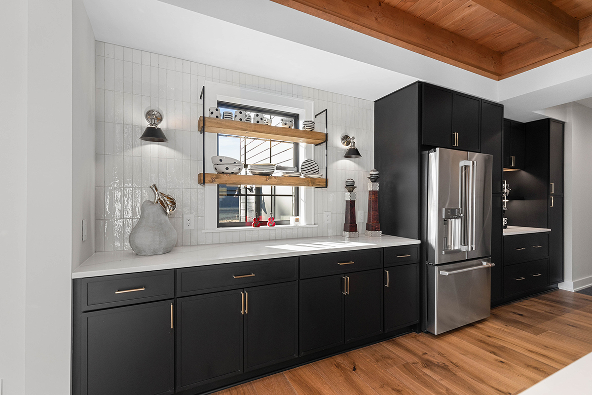 A kitchen with black cabinets and wood floors. The ceiling is exposed wooden beams that match the floor.