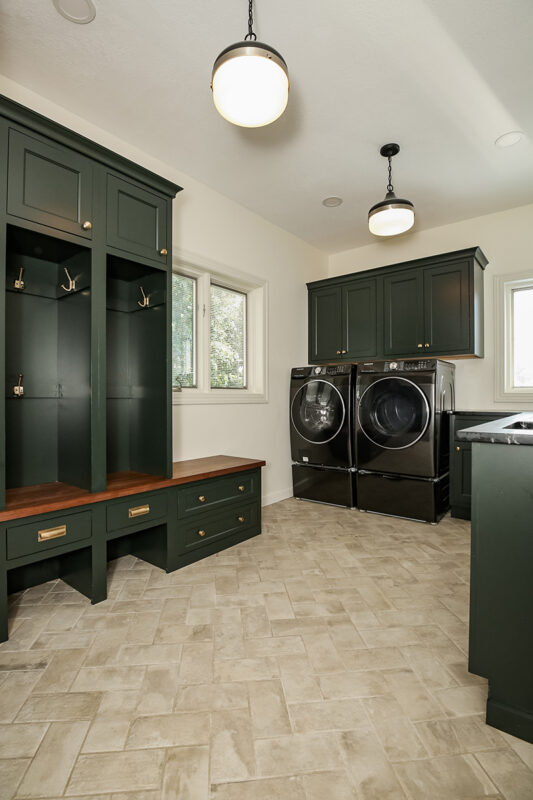green wooden cabinetry in laundry room. Washer and Dryer set tucked into the corner. Stone Flooring.