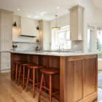 white kitchen cabinetry, with a brown wooden island and chair setup accompanied with a white marbled stone countertop.