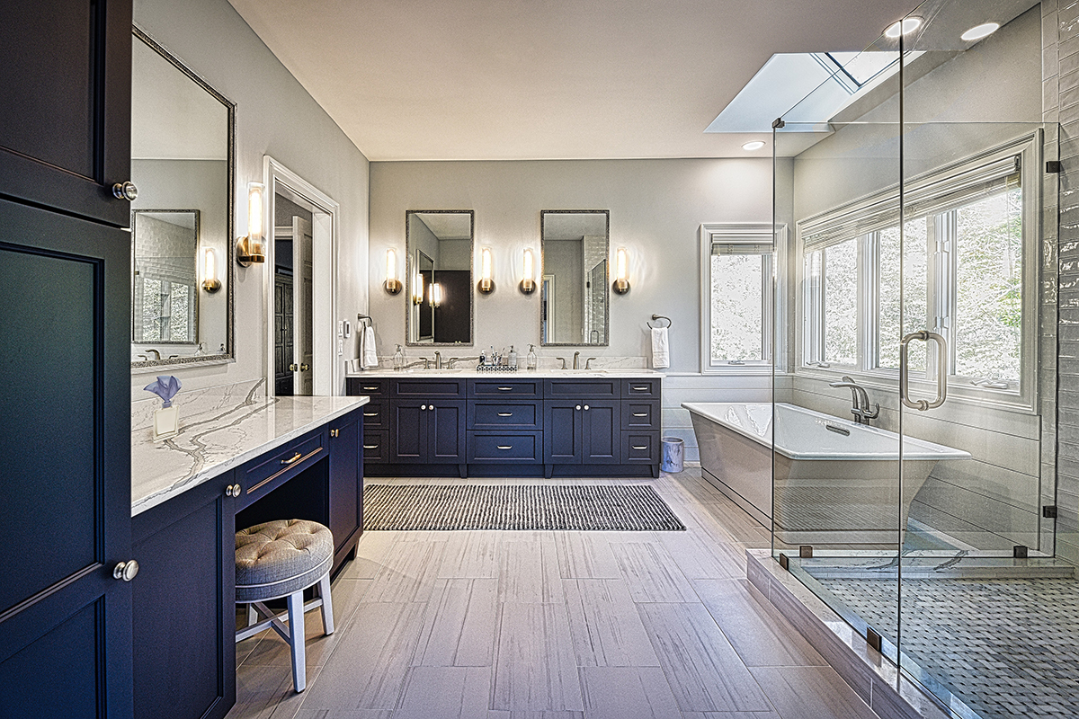 Shows soaking tub with glass shower and blue cabinets of a double vanity.