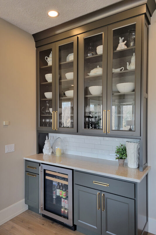 gray minibar with white tiled backsplash. glassware and drinks are inside the cabinets and fridge.