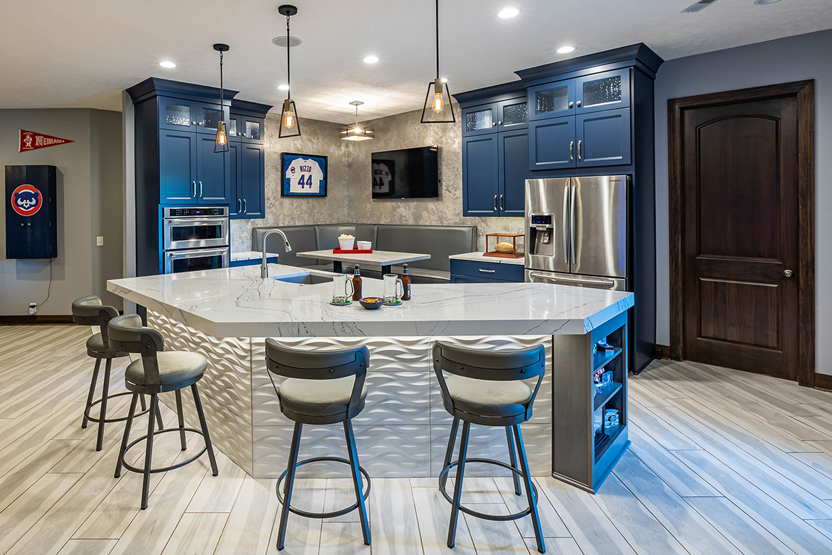 Shows a basement bar with blue cabinets. The bar top has a wavy grey feature under the countertop.