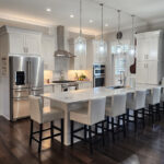 A large white kitchen; including a white island, white counter tops, and stainless steel appliances.