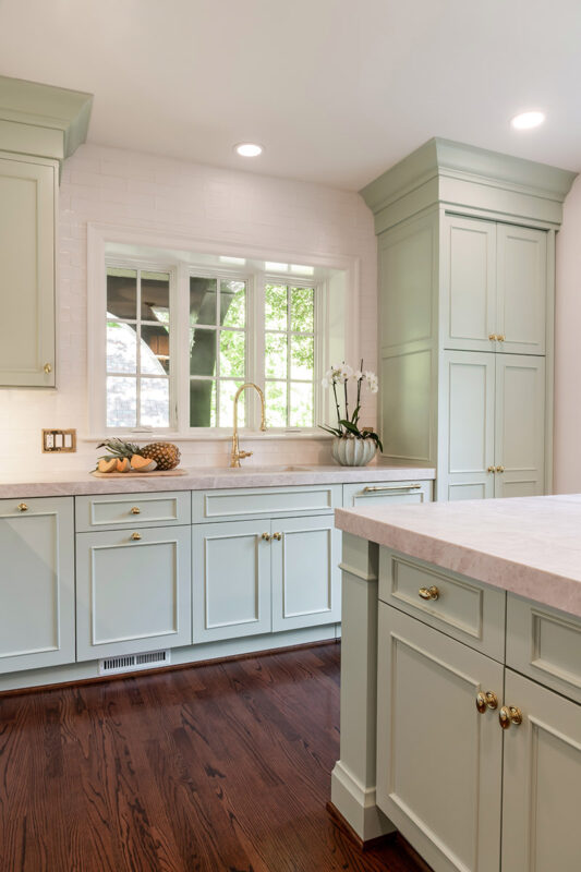 light green cabinets with gold hardware in kitchen, taupe countertops and sink
