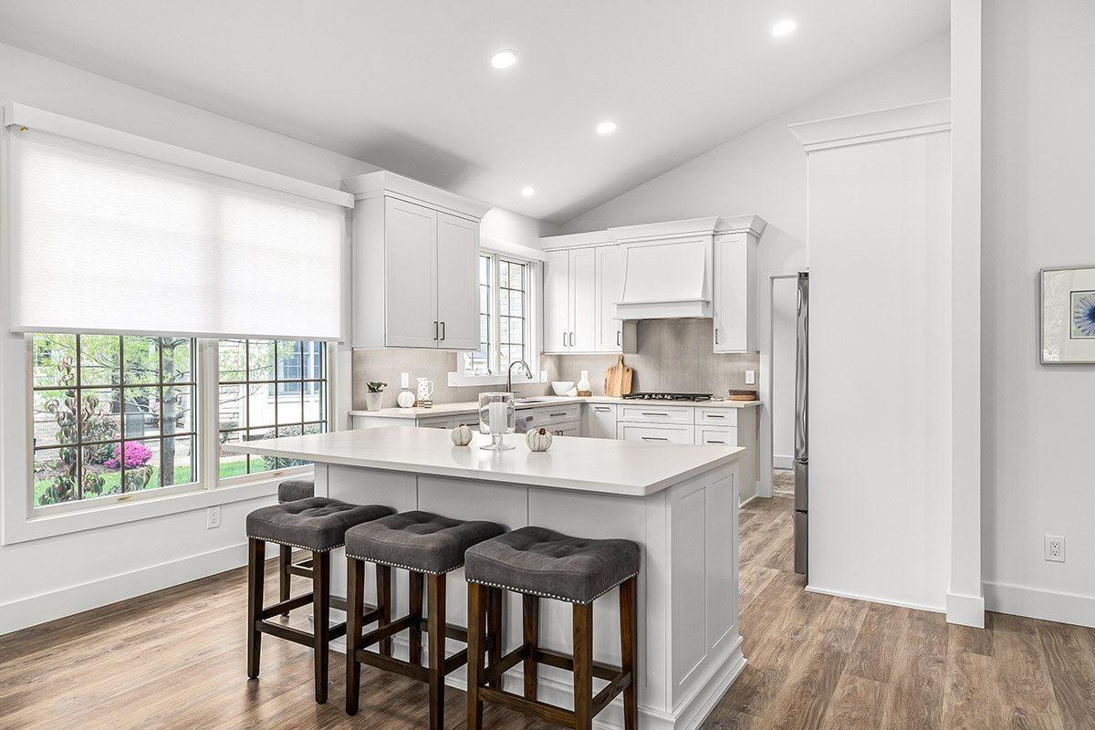 A wider view of the modern kitchen with sleek white cabinets. The island is located slightly outside of the kitchen work space and has bar seating.