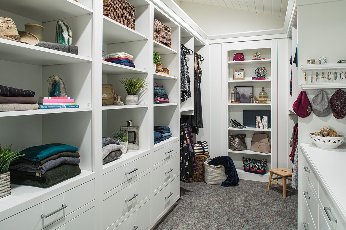 walk in closet with white cabinets and drawers, shelves are filled with clothes, plants, and other accessories.