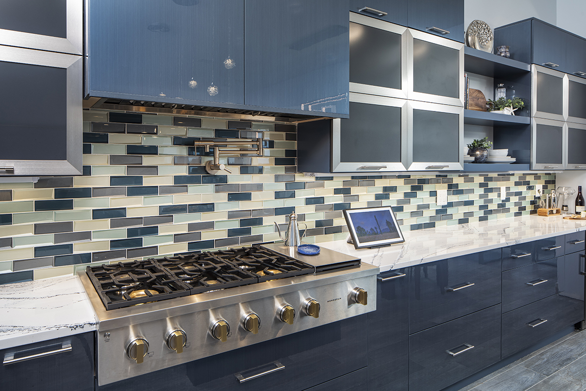 Multicolored tile backsplash accompanied with stainless steel appliances and glossy blue kitchen cabinetry.