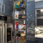 glossy blue acrylic kitchen cabinets showcasing a pantry drawer with various cooking ingredients. stainless steel appliances throughout.