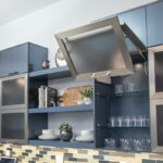 Grey modern cabinets that have doors that lift upward instead of sideways. The cabinets have a smoked glass on the front. The shelving instead of the cabinet is clear glass, but the body of the cabinet is a blue grey.