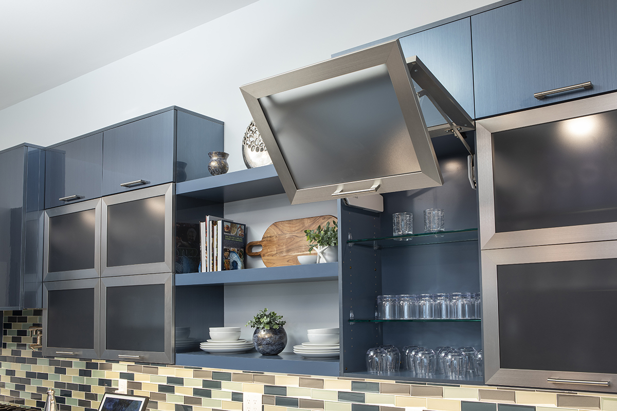 Grey modern cabinets that have doors that lift upward instead of sideways. The cabinets have a smoked glass on the front. The shelving instead of the cabinet is clear glass, but the body of the cabinet is a blue grey.