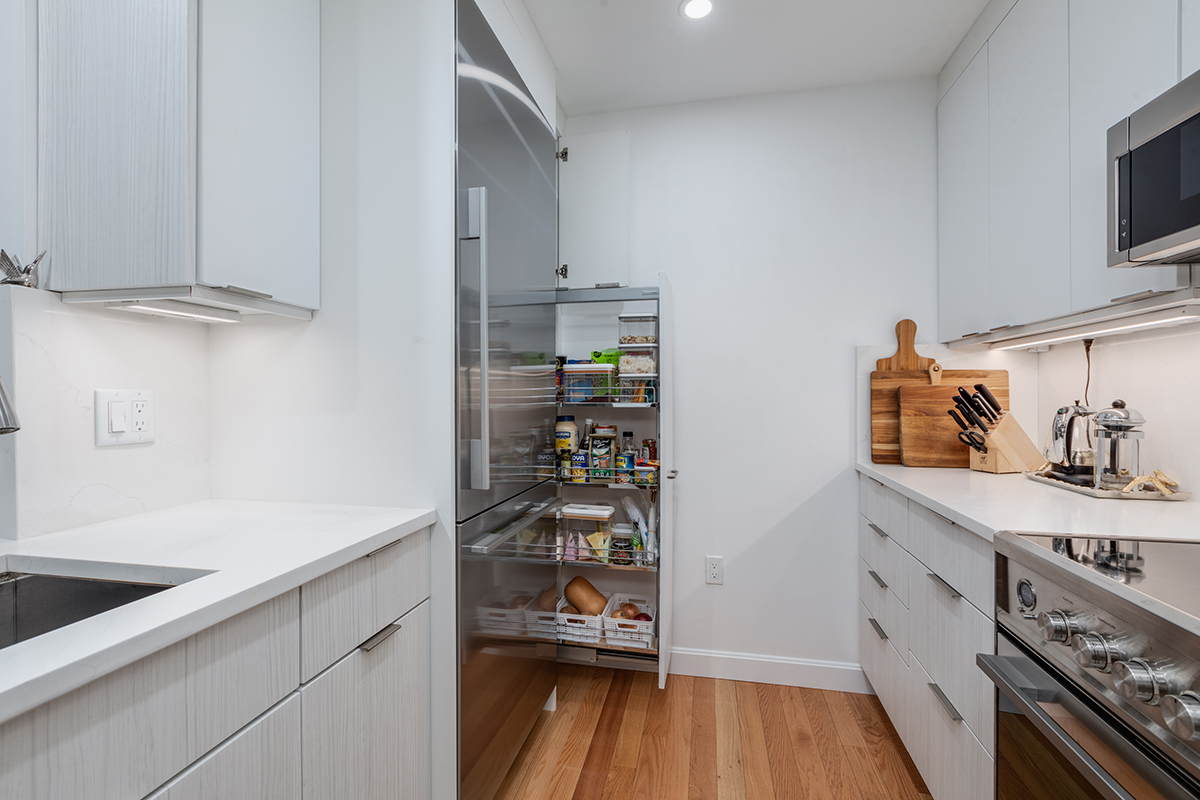 white kitchen with brushed gray cabinetry, showcasing stainless steel fridge and pull out pantry drawer.