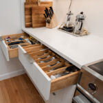 brushed white kitchen drawers and cabinets that hole silverware and cooking utensils.