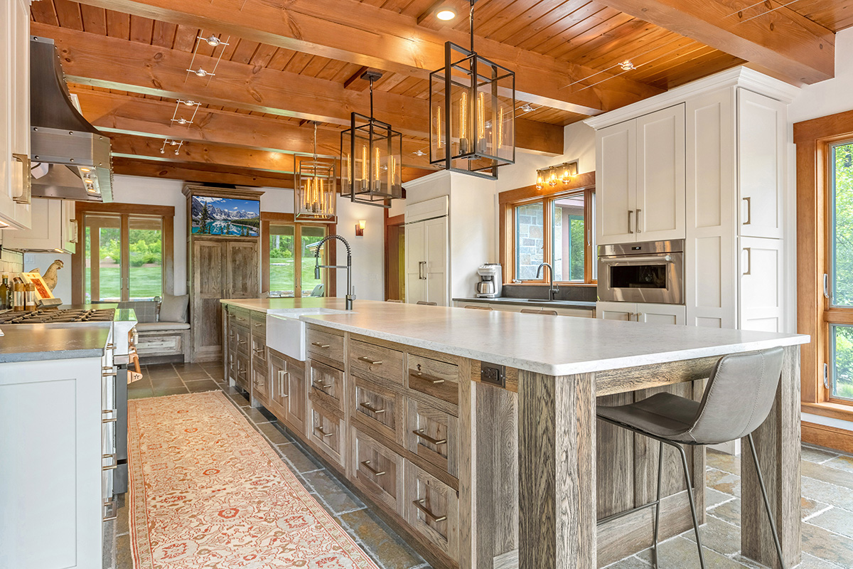 Ski house kitchen with grainy wooden cabinetry. White countertops and brushed copper accents. Wooden cabin styles throughout.