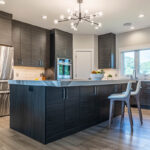 Brushed black wooden cabinetry in modern kitchen. Patterned stone countertops and stainless steel accessories.