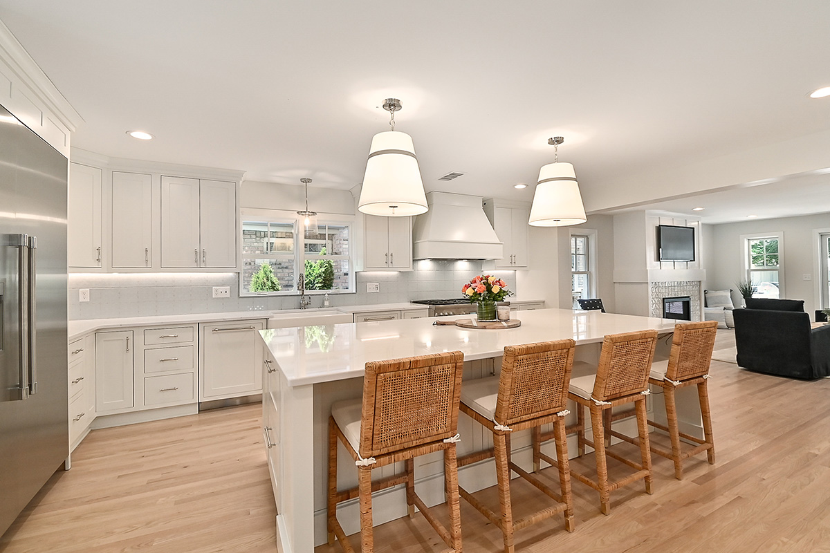 all white kitchen cabinetry with silver accents, and brown wicker chairs.