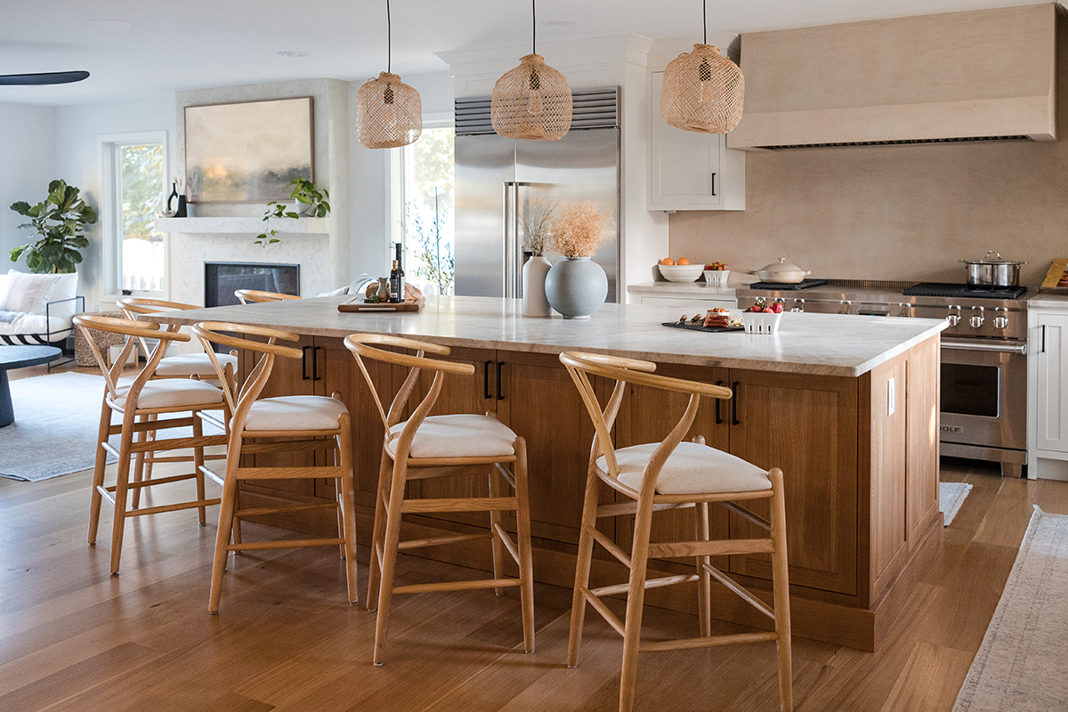 brown and white kitchen cabinetry. Large wooden island with stone countertops. Kitchen extends into living room. Stainless steel appliances.