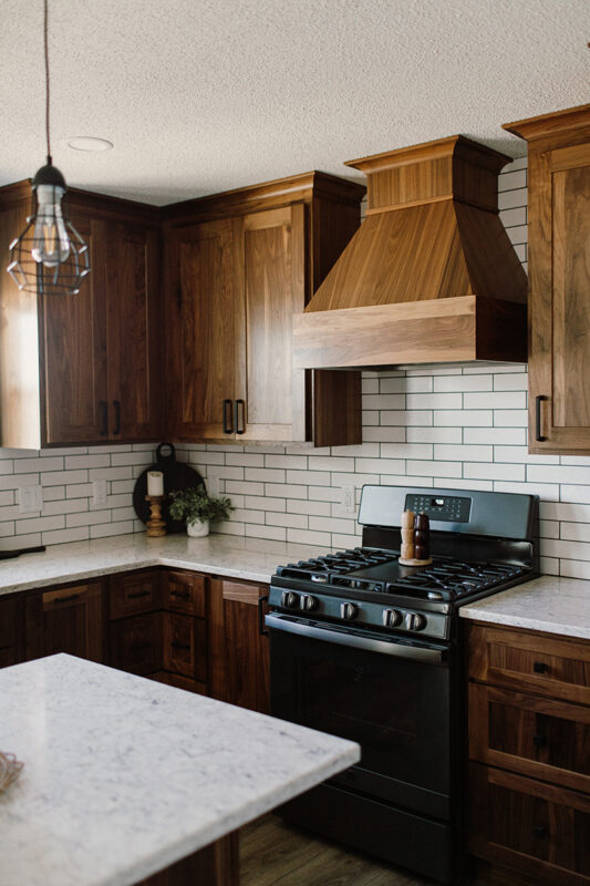 Kitchen that features brown, wood cabinets with a speckled white counter top. The stove and range are pictured, they are black.