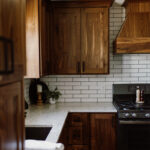 walnut cabinetry with stone countertop on tiled wall in kitchen.