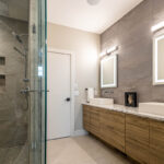 Wooden bathroom vanity with stone countertops. Rectangular LED mirrors sit on textured wall.
