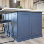 gray island cabinetry with white stone island countertop. Two leather chairs are tucked under the island.