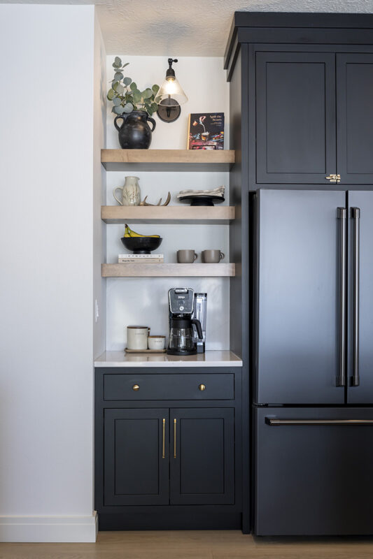 black cabinetry for coffee nook. Brown wooden shelves sit above. Brass accents on the handles and knobs.