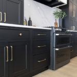 A close up of black cabinets on both sides of a stove. The cabinets have large gold handles.