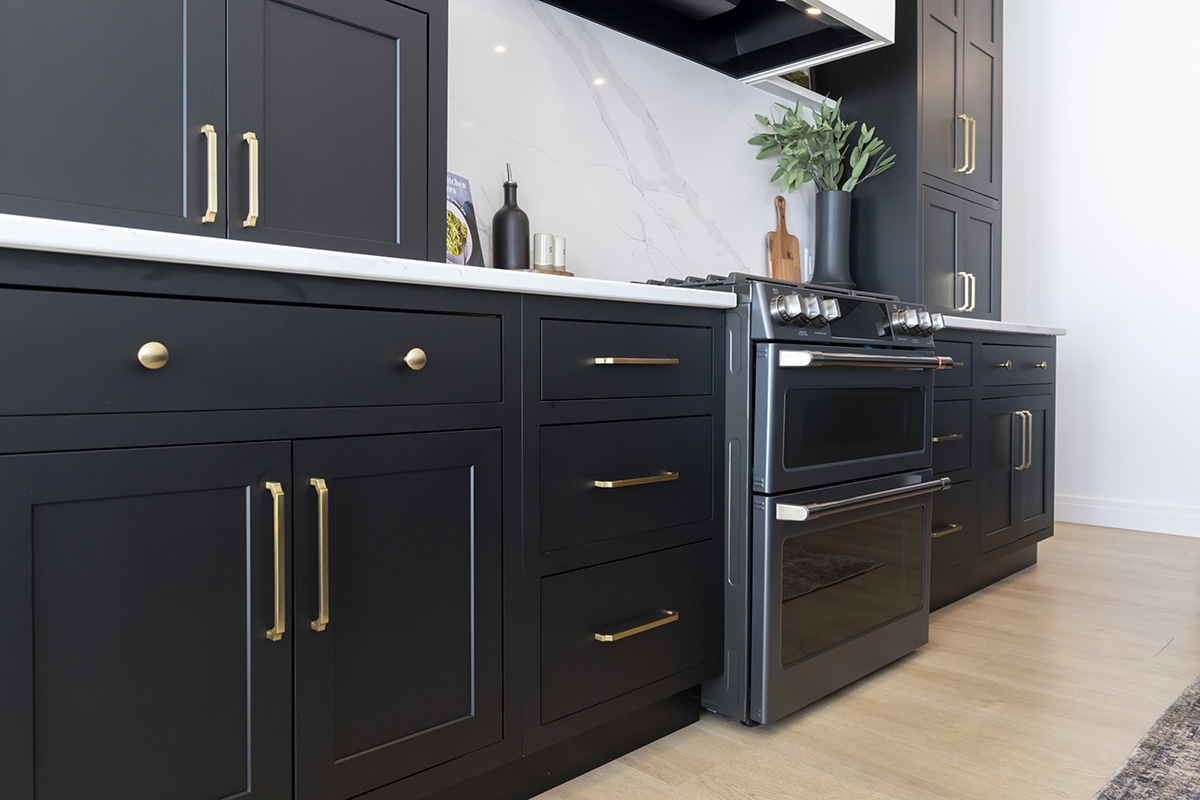 A close up of black cabinets on both sides of a stove. The cabinets have large gold handles.