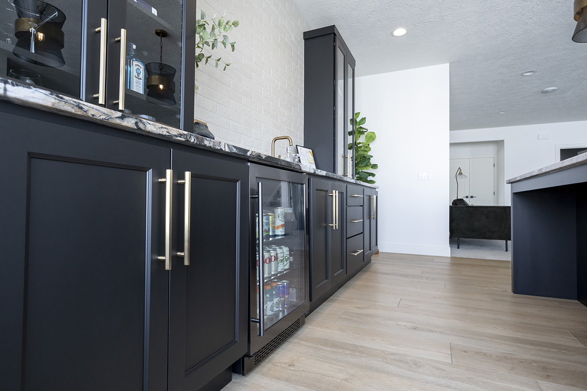 close up view of minibar with black cabinetry and silver accents. The mini fridge is stocked with beverages.