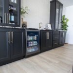 black minibar with marbled stone countertop. The cabinets are filled with beverages and glassware, and sit next to a white brick backsplash.