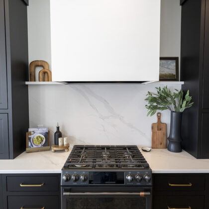 stove accompanied with black and gold cabinetry. white stone countertop and backsplash