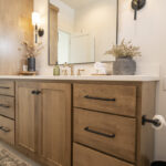 brown bathroom cabinetry with black accents. The white countertop holds a sink with gold accent handles and faucet.