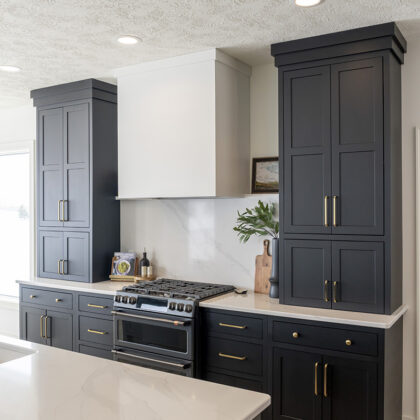 small black kitchen cabinetry with bronze handles. White countertops and white backsplash.