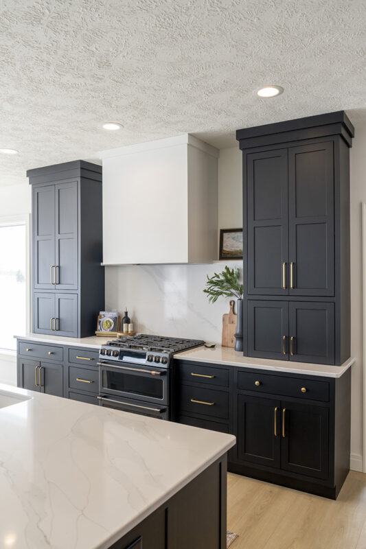 small black kitchen cabinetry with bronze handles. White countertops and white backsplash.