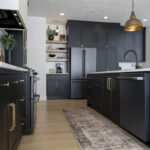Black kitchen cabinetry with gold accents. Dark appliances such as a fridge and dishwasher accompany cabinetry.