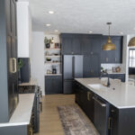black kitchen cabinetry with brass accents. White stone countertops.