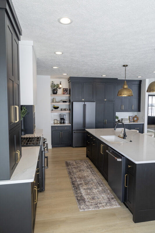 black kitchen cabinetry with brass accents. White stone countertops.