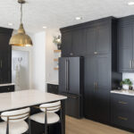 dark black kitchen cabinetry with dark gray appliances. White stone countertops including the stone island with white stools.