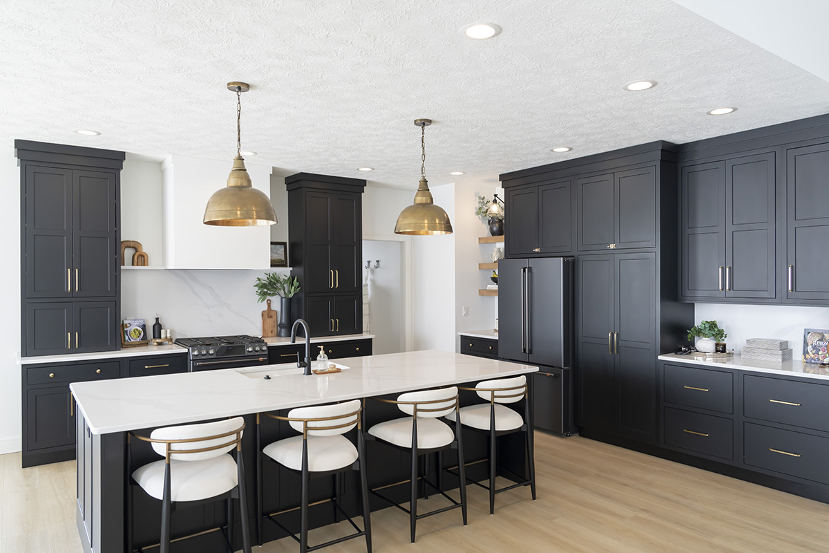 dark black kitchen cabinetry with gold accents. White island stone countertop with white stools.