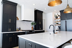 A modern kitchen with polished black cabinets, white countertops, and gold accents.