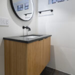 floating wood bathroom sink with gray countertop and large circular LED mirror.
