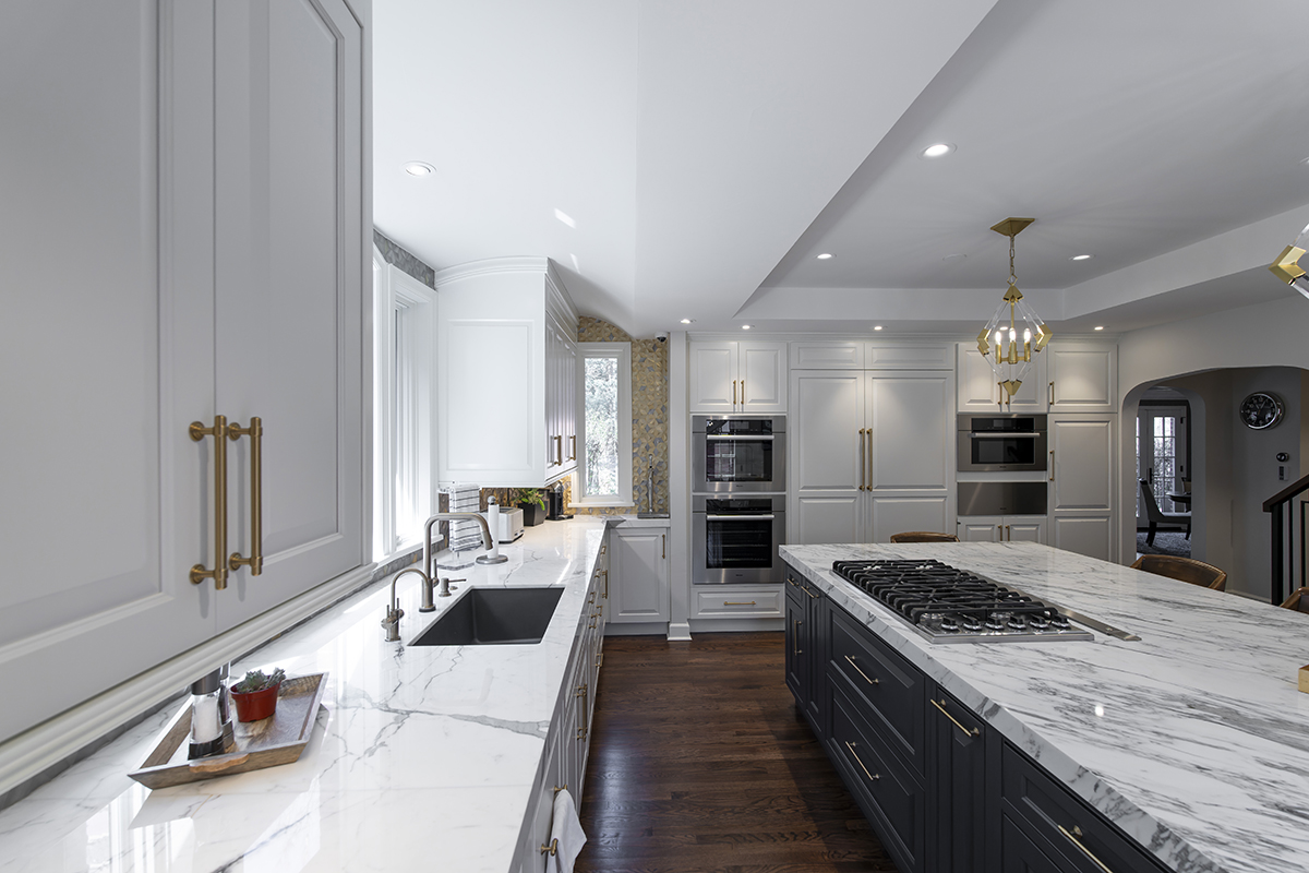 Modern kitchen with white stone countertops. Black and white wooden cabinets with golden accents scattered throughout the kitchen.