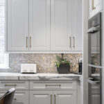 White kitchen cabinetry setup with brass accents accompanied by a textured intricate wall design.