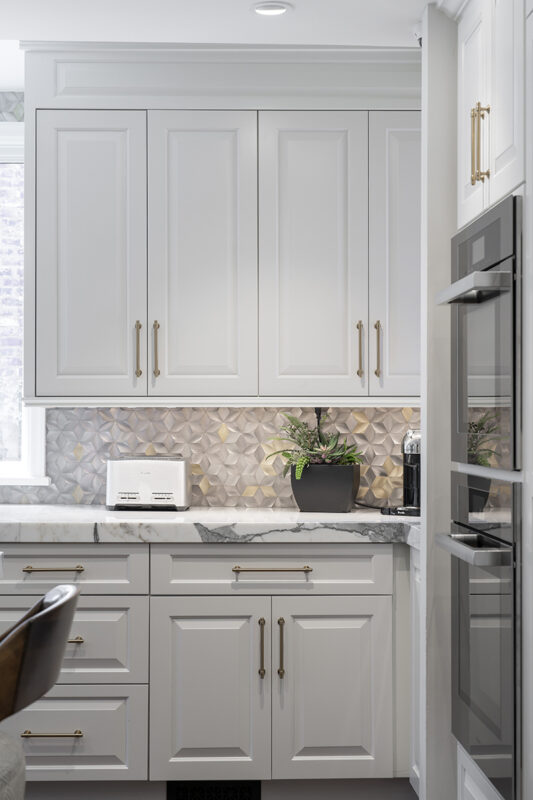 White kitchen cabinetry setup with brass accents accompanied by a textured intricate wall design.