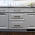 close up view of white kitchen cabinetry, and golden handles. Marbled white stone countertops.