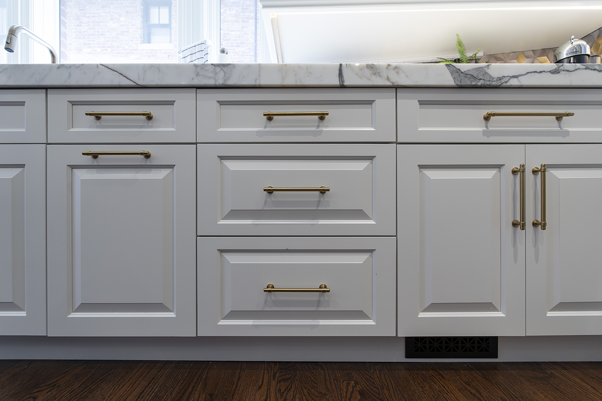 close up view of white kitchen cabinetry, and golden handles. Marbled white stone countertops.